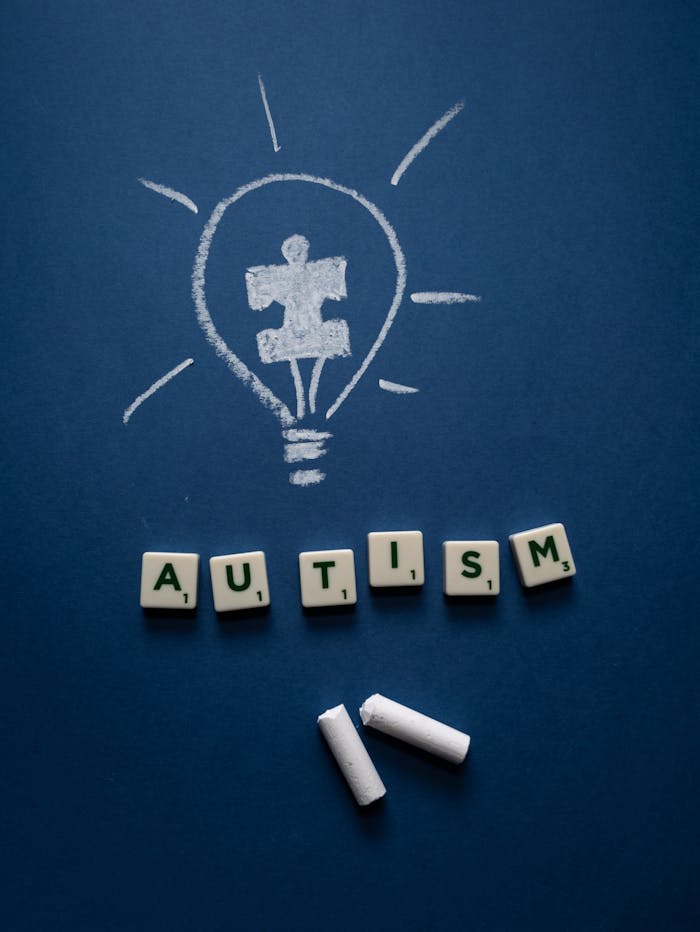 letter-tiles-and-chalks-on-a-blue-surface-8709146 Blue background with chalk-drawn puzzle light bulb and AUTISM letter tiles, promoting awareness.