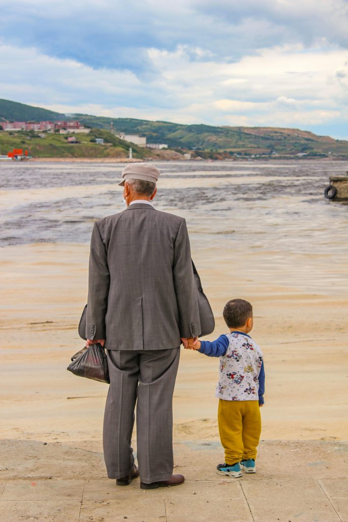 A senior man holds hands with a young boy, enjoying a peaceful moment by the water.